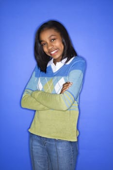 Portrait of African-American teen girl with arms crossed standing against blue background.