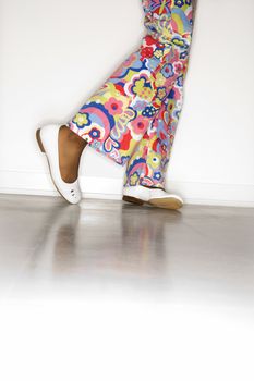Close-up of African-American teen girl's legs with floral pants and white shoes against white background.