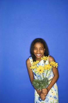 Portrait of African-American teen girl holding a bouquet of daisies standing in front of blue background.