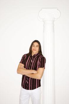Portrait of Asian-American teen boy standing with arms crossed leaning against column against white background.
