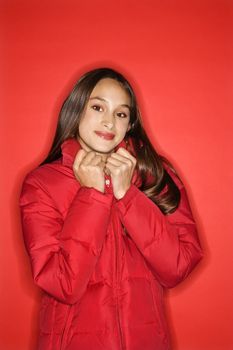 Portrait of Asian-American teen girl holding collar of her coat and smiling standing against red background.