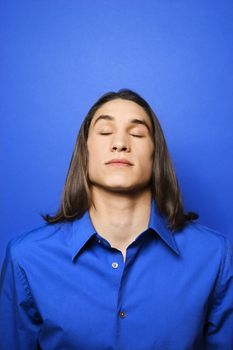 Portrait of Asian-American teen boy with eyes closed against blue background.