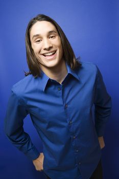 Portrait of Asian-American teen boy smiling at camera against blue background.