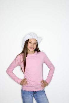 Portrait of Asian-American teen girl wearing cowboy hat and hands on hips standing against white background.