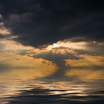 Sunset over water, with sunbeams trough heavy clouds.