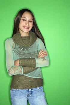 Portrait of smiling Asian-American teen girl with arms crossed standing in front of green background.