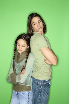 Portrait of Asian-American girl and teen boy standing back to back as boy looks down at girl over his shoulder.