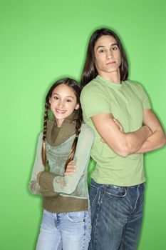 Portrait of Asian-American girl and teen boy standing back to back against green background.