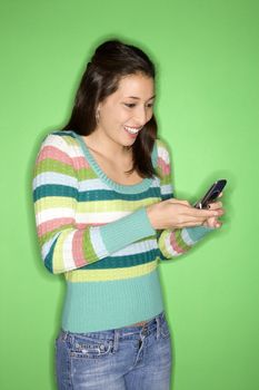 Portrait of smiling Multi-racial teen girl dialing cellphone standing in front of green background.