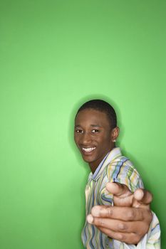 Portrait of smiling African-American teen boy holding hand out toward viewer against green background.