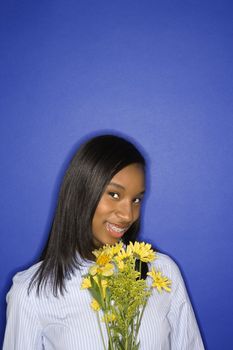 Portrait of smiling African-American teen girl with bouquet of flowers against blue background.