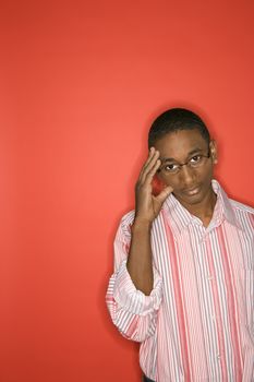 Portrait of African-American teen boy with glasses and hand on forehead against red background.