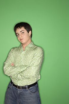 Portrait of Caucasian teen boy with crossed arms standing against green background.