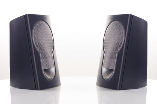 Two computer speakers, with a reflection on white background.