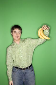 Portrait of smiling Caucasian teen boy holding bananas in air standing against green background.
