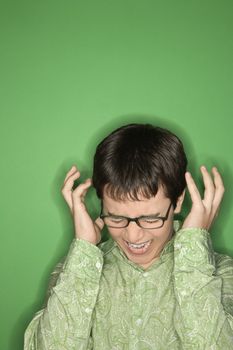 Portrait of Caucasian teen boy screaming with hands beside ears in front of green background.