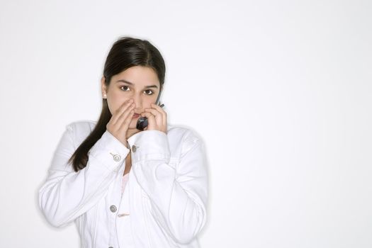 Portrait of Caucasian teen girl whispering into cellphone standing against white background.