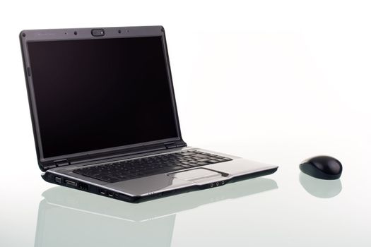 A modern laptop computer and wireless mouse with reflection on a glass surface.