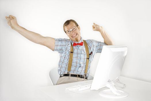 Young Caucasian man smiling and stretching arms out at computer.