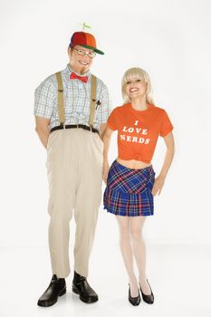 Caucasian young man dressed like nerd wearing propeller hat with Caucasian blonde young woman wearing tshirt reading I love nerds and plaid skirt.