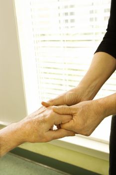 Caucasian female nurse massaging arthritic hands of elderly man at retirement community center.
