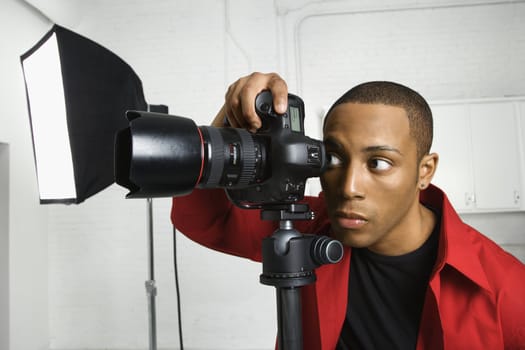 African American young male adult looking through camera on tripod.