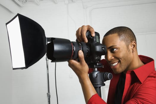 African American young male adult looking through camera on tripod.