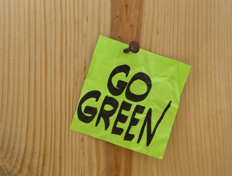 go green reminder - green crumpled sticky note nailed to a wood plank or wall