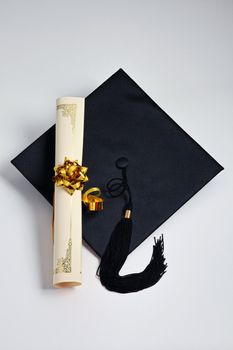 Graduation cap and diploma on the plain background

