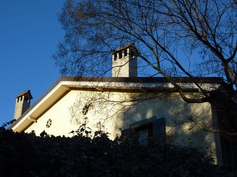 Sunny facade and roof of a house with chimneys and trees around