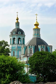 a photo of an Orthodox Church with green walls and golden domes stand behind the trees