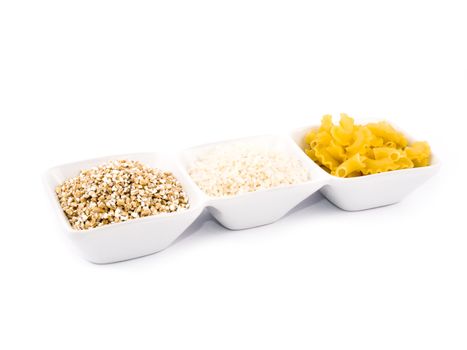 Three porceline bowls filled with pasta, groats and rice, on white background