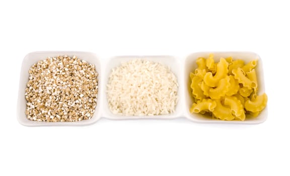 Three porceline bowls filled with pasta, groats and rice, on white background