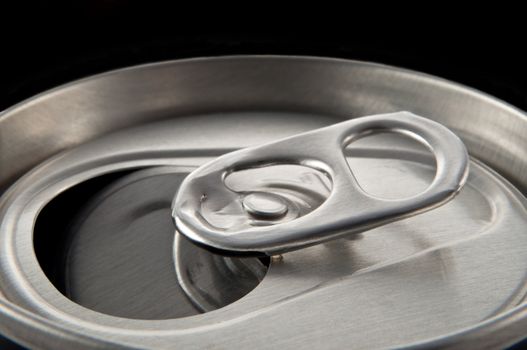 Close and low level angle capturing an aluminium can ring pull against black background.