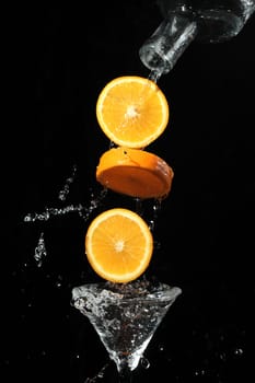 The segments of fruit falling in a glass with a drink
