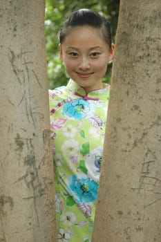 Chinese girl standing between trees in park.