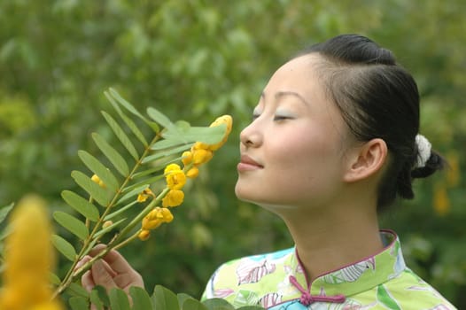 Chinese girl in park, smelling flowers.