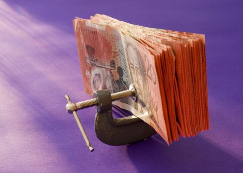 a wad of australian 20 dollar notes pressed in a G clamp