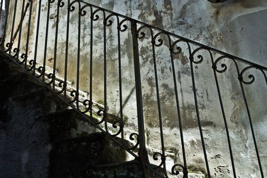 Old italian iron banister with stone stairs and decayed wall