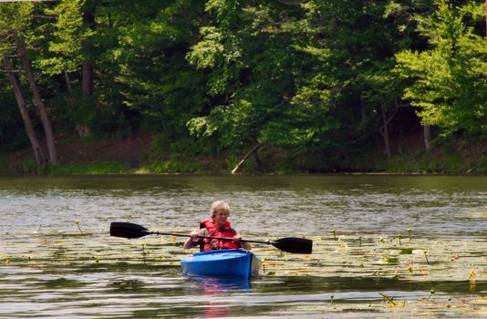 Female senior citizen kayaking on a pond - active retirement.