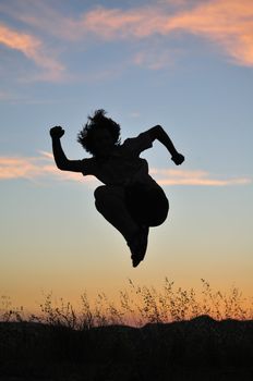 Man jumps high above tall grasses in front of a fiery sunset.