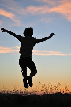 Man jumps above tall grasses in front of a fiery sunset.