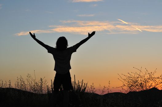 Man stands triumphant at sunset among the silhouettes of tall grasses.