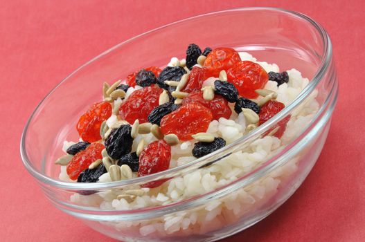 Boiled White Rice with Dried Fruit and Sunflower Seeds in Transparent Bowl on Red Background