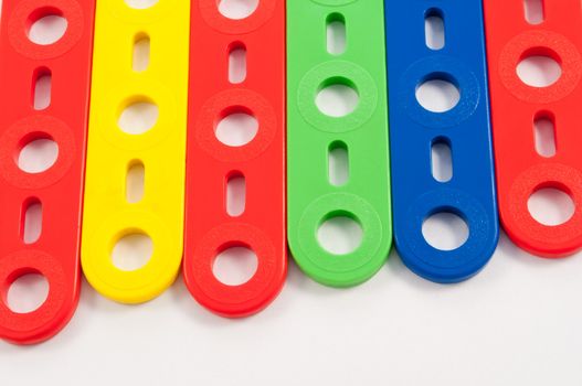 Close up capturing components from a brightly coloured child's construction set arranged over white.