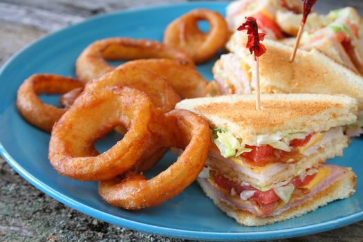 Ham and Turkey club sandwich with onion rings on a blue plate.