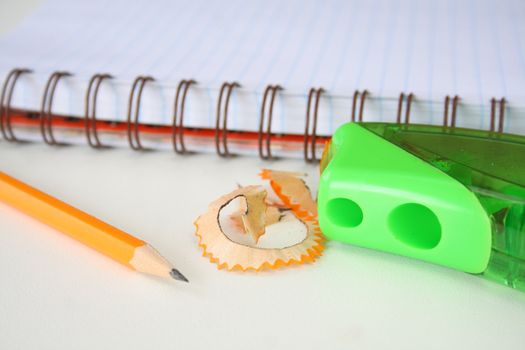 Pencil and sharpner with shavings and a notebook in the background.
