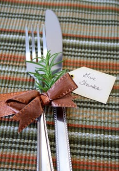 Eatting ustensils wraped in a bronze bow with a fresh twig of Rosemary and a tag with the words Give Thanks.  Shallow DOF used with focus on the bow and rosemary.