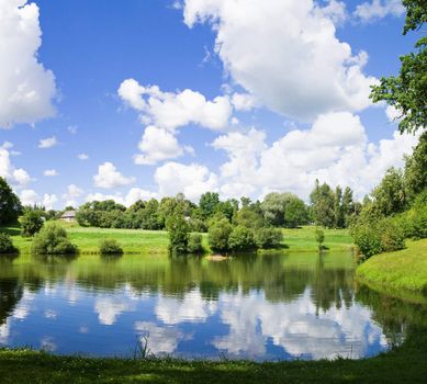 Summer scenery with lake in front, green forest on back with blue sky and clouds