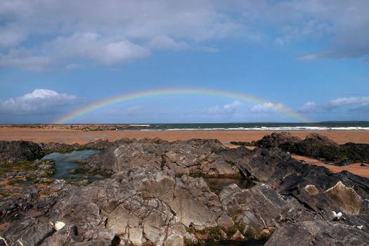 a rocky beach on a warm wet day with a calm sea and a rainbow after a shower an ideal place to have a walk in ireland